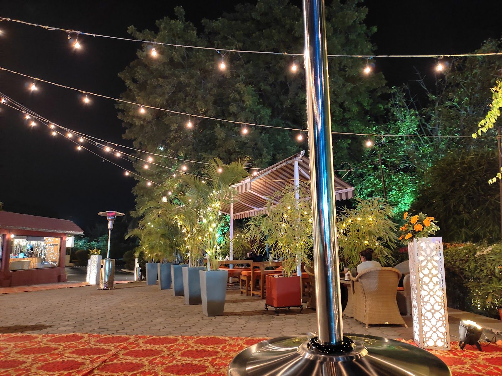 The lawn at night under strings of warm lights, with outdoor heaters and potted palms